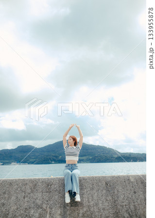 海に向かって両手を広げる20代女性。旅先で感じる自由と解放のエモーショナルな時間 133955878