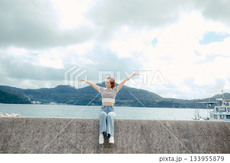 海に向かって両手を広げる20代女性。旅先で感じる自由と解放のエモーショナルな時間 133955879