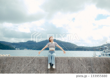 海に向かって両手を広げる20代女性。旅先で感じる自由と解放のエモーショナルな時間 海に向かって両手を広げる20代女性。旅先で感じる自由と解放のエモーショナルな時間 133955880