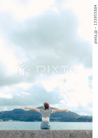 海に向かって両手を広げる20代女性。旅先で感じる自由と解放のエモーショナルな時間 海に向かって両手を広げる20代女性。旅先で感じる自由と解放のエモーショナルな時間 133955884