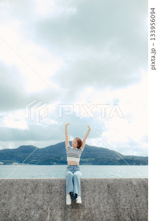 海を背景にスマホを構える20代女性。旅先で思い出を切り取るエモーショナルな時間 海を背景にスマホを構える20代女性。旅先で思い出を切り取るエモーショナルな時間 133956094