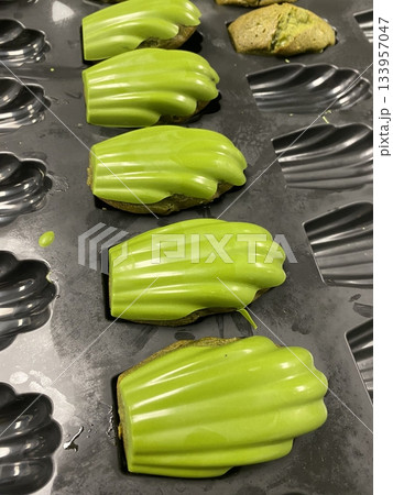 Matcha madeleine cake with soft, fluffy texture and delicate shell shape, coated with a light dusting of vibrant green matcha powder, highlighting its smooth surface and elegant detail 133957047