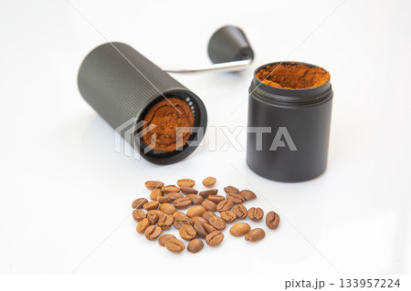 A black manual coffee grinder, disassembled, reveals freshly ground coffee 133957224