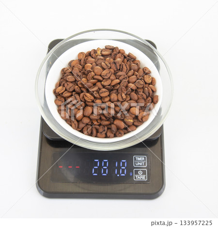 A glass bowl filled with roasted coffee beans sits on a digital scale A glass bowl filled with roasted coffee beans sits on a digital scale 133957225
