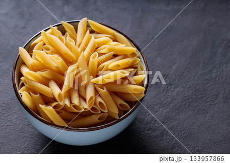 Uncooked Penne Pasta in Bowl on Dark Stone Background Copy Space Uncooked Penne Pasta in Bowl on Dark Stone Background Copy Space 133957866