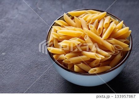 Uncooked Penne Pasta in Bowl on Dark Stone Background Copy Space 133957867