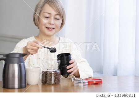 リビングでコーヒー豆を挽いてコーヒーを飲んで寛ぐシニア女性 リビングでコーヒー豆を挽いてコーヒーを飲んで寛ぐシニア女性 133960811