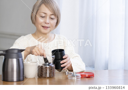 リビングでコーヒー豆を挽いてコーヒーを飲んで寛ぐシニア女性 133960814