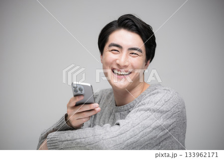 スマホを見るハンサムな男性　グレーバックカメラ目線笑顔 133962171