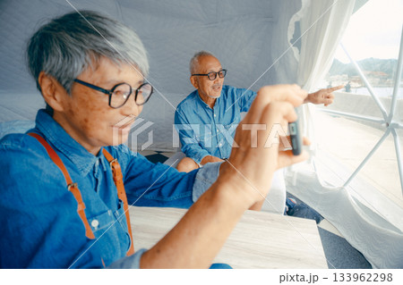 グランピング施設でスマホ撮影を楽しむシニア夫婦 133962298