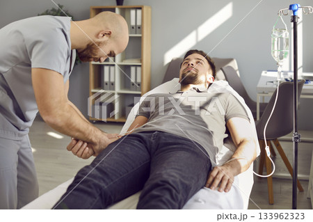 Nurse puts intravenous vitamin infusion catheter in vein of young male patient on bed Nurse puts intravenous vitamin infusion catheter in vein of young male patient on bed 133962323
