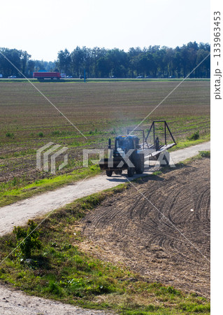 Harvester prepares postharvest cleanup, Lone tractor crosses stubbled land at sunset 133963453