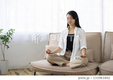 ソファの上で座禅を組み目を閉じて瞑想する女性 133963802