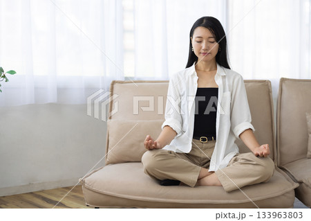 ソファの上で座禅を組み目を閉じて瞑想する女性 133963803