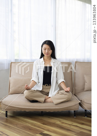 ソファの上で座禅を組み目を閉じて瞑想する女性 133963804
