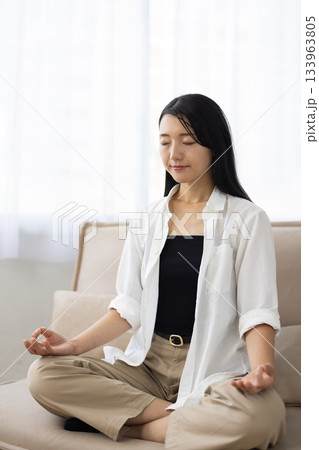 ソファの上で座禅を組み目を閉じて瞑想する女性 133963805