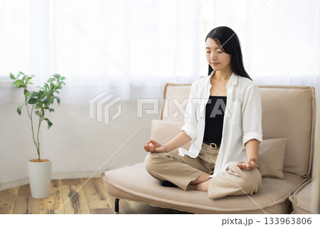 ソファの上で座禅を組み目を閉じて瞑想する女性 133963806