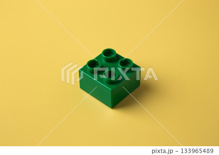 Green plastic building toy block on yellow background 133965489