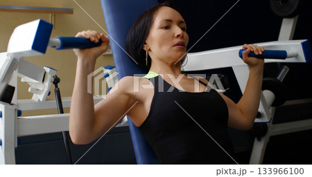 Caucasian woman in excellent physical shape during training in the gym. Deltoid press. Physical education as a norm of life to maintain health. Close-up photo. Caucasian woman in excellent physical shape during training in the gym. Deltoid press. Physical education as a norm of life to maintain health. Close-up photo. 133966100