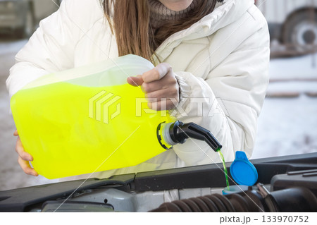A person is pouring bright yellow windshield washer fluid into their vehicles reservoir to prepare for winter driving A woman pours a yellow washer or antifreeze into her car in winter on the street A person is pouring bright yellow windshield washer fluid into their vehicles reservoir to prepare for winter driving A woman pours a yellow washer or antifreeze into her car in winter on the street 133970752
