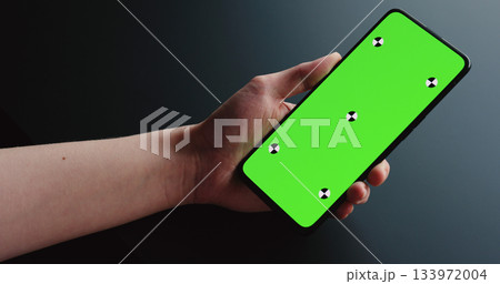 young woman sitting at the black table near window and holding smartphone with vertical green screen young woman sitting at the black table near window and holding smartphone with vertical green screen 133972004
