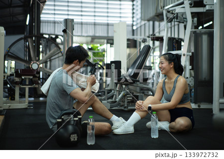 A trainer and a woman take a break after exercising, talking and cooling down together at the gym 133972732