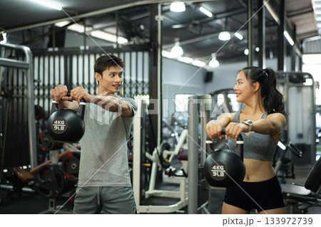 Fit and muscular man and woman focused on lifting a kettlebell during an exercise class 133972739