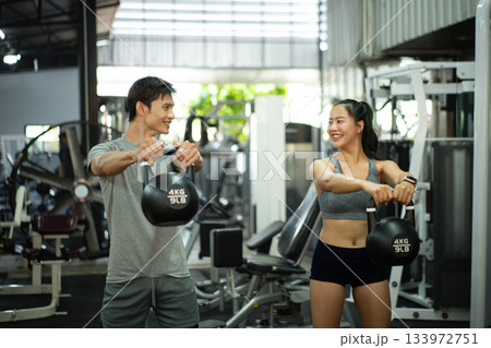 Fit and muscular man and woman focused on lifting a kettlebell during an exercise class Fit and muscular man and woman focused on lifting a kettlebell during an exercise class 133972751