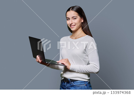 Portrait of smiling teenage girl holding laptop on gray studio background Portrait of smiling teenage girl holding laptop on gray studio background 133974368