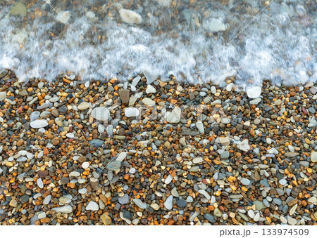 Sea wave washing over a shore covered with multicolored pebbles 133974509