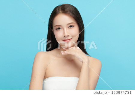 A beautiful young Asian woman with clean, fresh skin against a blue background. Skincare, facial treatment, cosmetology, beauty, and spa. An elegant portrait of an Asian woman. 133974751