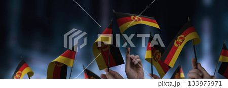 GDR flags in their hands on a blurred urban background GDR flags in their hands on a blurred urban background 133975971