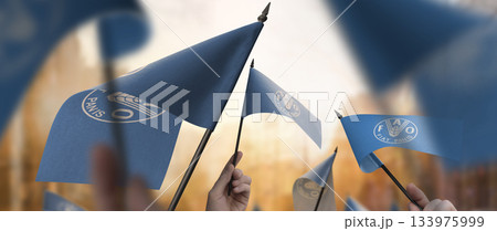 Food and agriculture organization flags in their hands on a blurred urban background Food and agriculture organization flags in their hands on a blurred urban background 133975999