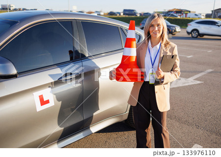 Driving Instructor Holding Cones Beside Training Car in Parking Lot 133976110