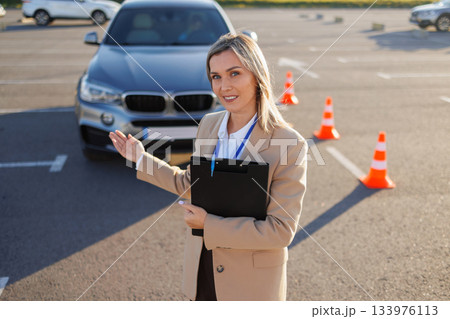 Driving Instructor Standing by Car on Training Course with Cones Driving Instructor Standing by Car on Training Course with Cones 133976113