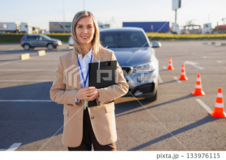 Instructor Standing by Learner Car with L Plate and Traffic Cones 133976115