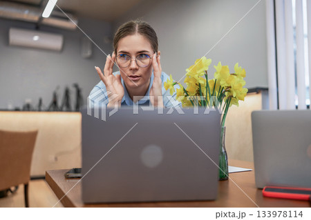 Woman laptop office professional adjusting glasses intensely focusing on computer screen near flowers Woman laptop office professional adjusting glasses intensely focusing on computer screen near flowers 133978114