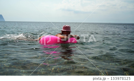 Beach water summer: Child swims with pink floatation aid in ocean near shore for vacation fun. 133978125