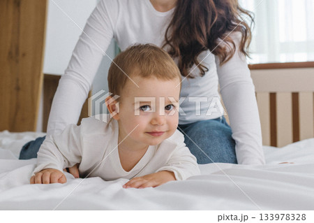 Young mother playing with her baby at home, enjoying a warm and cozy family moment full of tenderness, comfort, natural light, and playful parent-child connection. Young mother playing with her baby at home, enjoying a warm and cozy family moment full of tenderness, comfort, natural light, and playful parent-child connection. 133978328