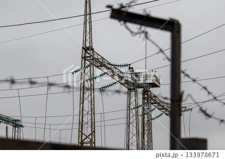 Electric towers rise above the ground, with wires running between them, surrounded by a security fence on a cloudy day 133978671