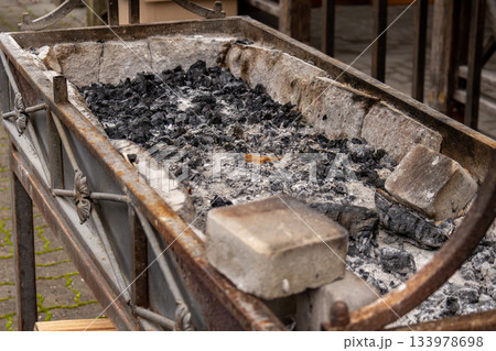 The charcoal grill shows ash and burnt remnants after being used for cooking food during a gathering in a market square The charcoal grill shows ash and burnt remnants after being used for cooking food during a gathering in a market square 133978698