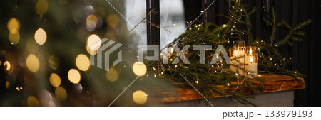Banner christmas tree branches with golden lights and ornaments in cozy dark room Banner christmas tree branches with golden lights and ornaments in cozy dark room 133979193