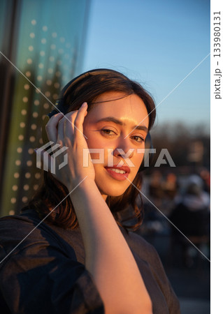 Young woman enjoying music at sunset in an urban environment with headphones on, radiating joy and relaxation 133980131