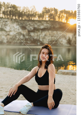 Woman practicing yoga at sunset by the lake in a serene outdoor setting surrounded by nature and mountains Woman practicing yoga at sunset by the lake in a serene outdoor setting surrounded by nature and mountains 133980760