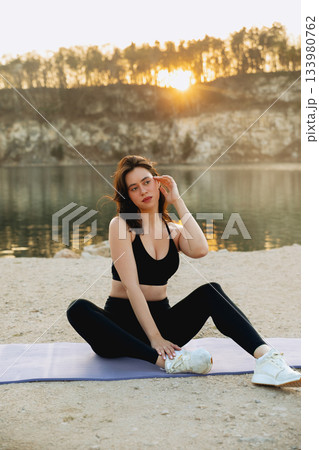 Woman practices yoga at sunset by a calm lake, showcasing tranquility and connection with nature during outdoor exercise 133980762