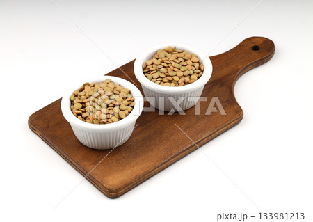 Green lentils in wooden bowl on isolated white background. Top view, copy space. Flat lay. Green lentils in wooden bowl on isolated white background. Top view, copy space. Flat lay. 133981213
