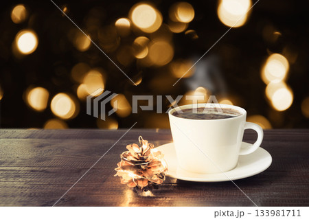 Hot coffee with steam in white cup on rustic wooden table, golden bokeh lights background. Christmas atmosphere, cozy evening winter concept. Hot coffee with steam in white cup on rustic wooden table, golden bokeh lights background. Christmas atmosphere, cozy evening winter concept. 133981711