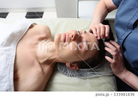 Facial massage. A young woman does facial skin care in a beauty salon. The concept of beauty. Facial massage. A young woman does facial skin care in a beauty salon. The concept of beauty. 133981836