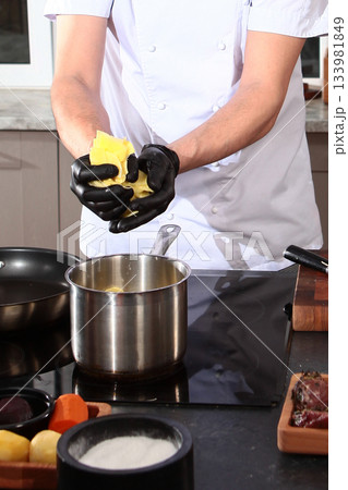 The cook in the kitchen holds sliced potatoes in his hands. Sliced potatoes in the hands of the cook. Cooking dishes from vegetables. Hands in protective glove The cook in the kitchen holds sliced potatoes in his hands. Sliced potatoes in the hands of the cook. Cooking dishes from vegetables. Hands in protective glove 133981849