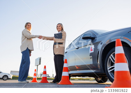 Driving Instructor and Student Celebrating New License with Car in Background 133981922